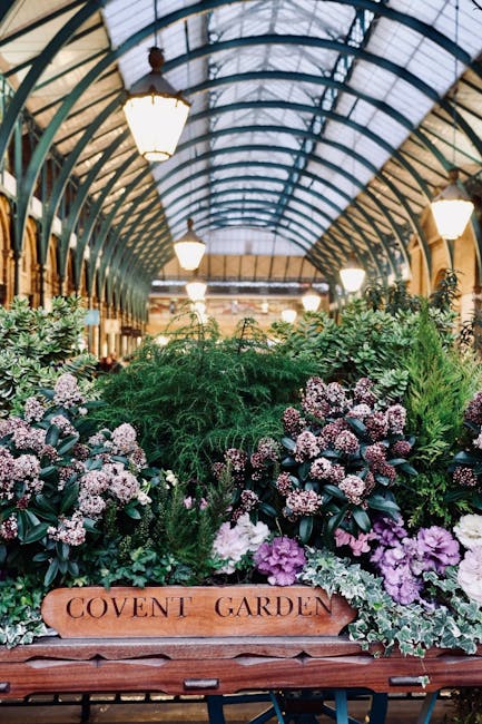 Inside a large indoor marketplace with a high, arched glass ceiling supported by blue-tinted metal framework, the scene shows a busy public space filled with people walking and standing throughout. On